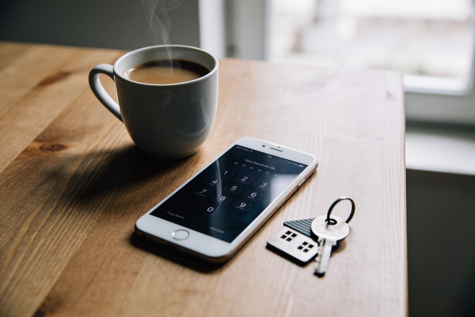 Un téléphone posé sur une table, écran verrouillé, à côté d'une tasse